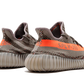 L'Adidas Yeezy Boost 350 V2 "Carbon Beluga" unisce vividi tocchi di colore con un design fantasia. I lacci in corda fissano la tomaia Primeknit traspirante, resa in una finitura grigio scuro con linee nere ondulate e macchioline arancioni a contrasto. Sul lato laterale, una striscia arancione abbinata mostra il marchio "SP