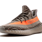 L'Adidas Yeezy Boost 350 V2 "Carbon Beluga" unisce vividi tocchi di colore con un design fantasia. I lacci in corda fissano la tomaia Primeknit traspirante, resa in una finitura grigio scuro con linee nere ondulate e macchioline arancioni a contrasto. Sul lato laterale, una striscia arancione abbinata mostra il marchio "SP